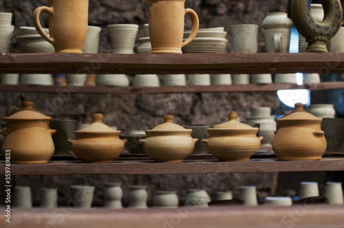 Wooden racks in a pottery workshop in which there are pottery, many different pottery standing on the shelves in a pottery workshop. Master crock. Inside interior. Low light