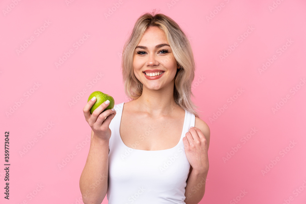 Teenager blonde girl over isolated pink background with an apple and happy Teenager blonde girl over isolated pink background with an apple and happy