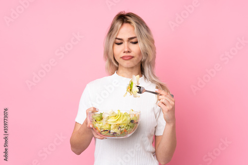 Teenager blonde girl holding a salad over isolated pink wall