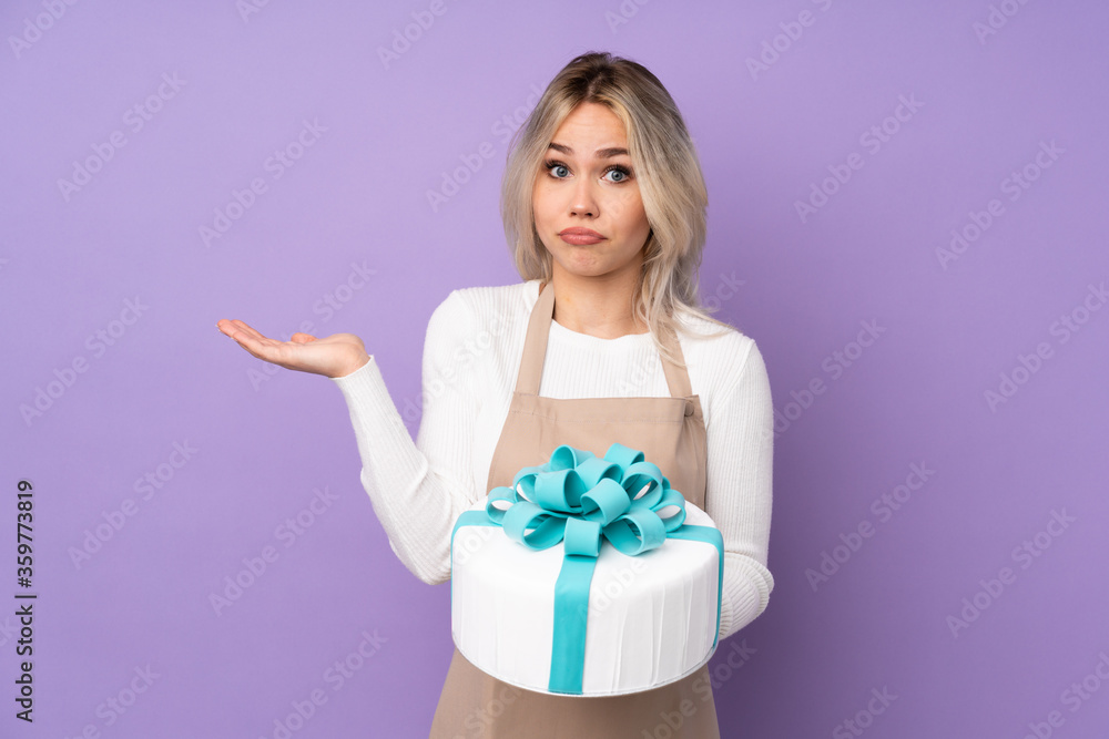 Young pastry chef holding a big cake over isolated purple background having doubts with confuse face expression Young pastry chef holding a big cake over isolated purple background having doubts with confuse face expression