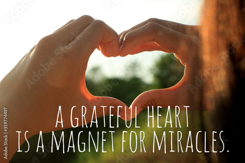 Inspirational quote  - A grateful heart is a magnet for miracles. With young woman hands making love sign against the sunset light. Thankfulness and gratefulness inspiration words concept. photo