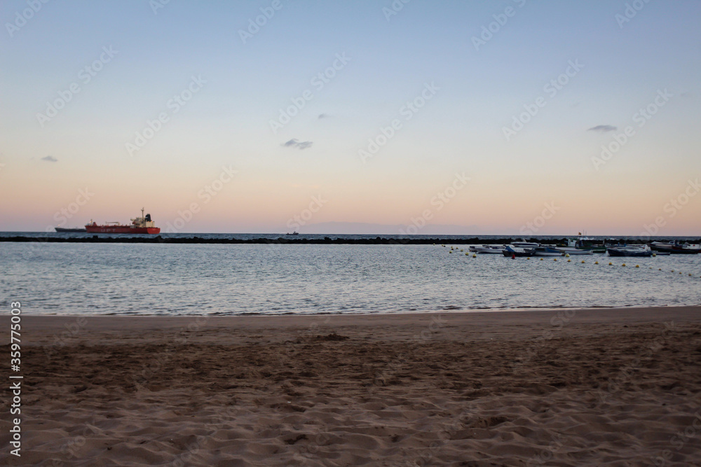 A beach at sunset with a ship in the background A beach at sunset with a ship in the background