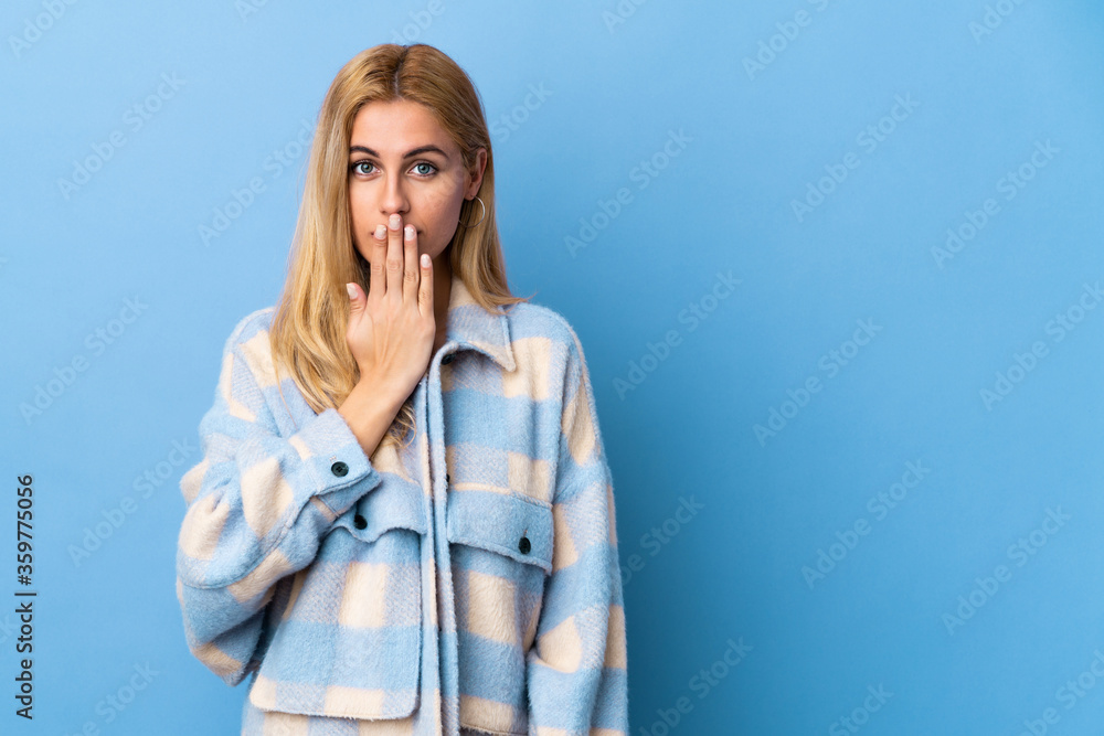 Young Uruguayan blonde woman over isolated background covering mouth with hand Young Uruguayan blonde woman over isolated background covering mouth with hand