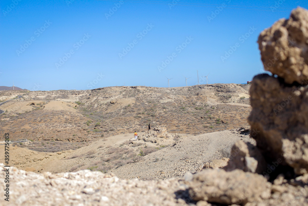A dry mountain range in Tenerife, spain against a clear blue sky in the background with a pile of rocks out of focus in the foreground