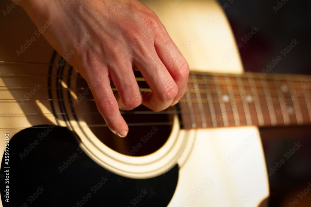 Fototapeta premium Close up photo of a girl plays the guitar at home. Warm evening sunlight and yellow tones. self-development at home