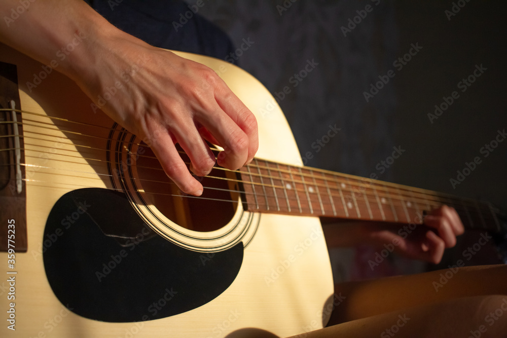 Fototapeta premium girl plays the guitar at home. Warm evening sunlight and yellow tones. self-development at home
