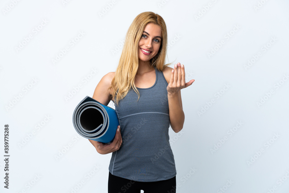 Young sport woman going to yoga classes while holding a mat over isolated white background inviting to come with hand. Happy that you came Young sport woman going to yoga classes while holding a mat over isolated white background inviting to come with hand. Happy that you came