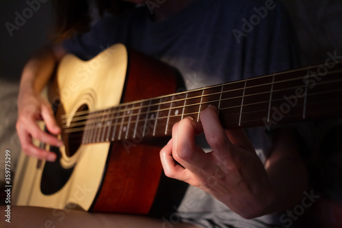 Close up photo of a girl plays the guitar at home. Warm evening sunlight and yellow tones. self-development at home