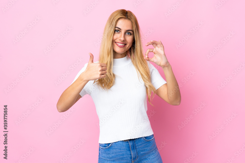 Young Uruguayan blonde woman over isolated pink background showing ok sign and thumb up gesture Young Uruguayan blonde woman over isolated pink background showing ok sign and thumb up gesture