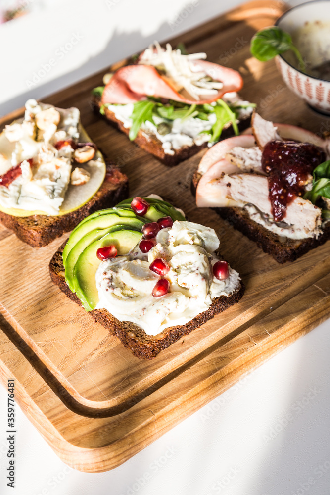 Four different rye bread open sandwiches (avocado-quail eggs, pear-gorgonzola, ham-cheese, turkey-apple) and bowl with mustard sauce on wooden board on white background. Four different rye bread open sandwiches (avocado-quail eggs, pear-gorgonzola, ham-cheese, turkey-apple) and bowl with mustard sauce on wooden board on white background.