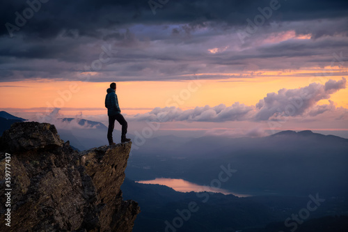 Fantasy Adventure Composite with a Man on top of a Mountain Cliff with Dramatic Landscape in Background during Sunset or Sunrise. Landscape from British Columbia  Canada.