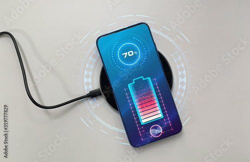 The black mobile phone is on wireless charging, on a white background. Futuristic phone is charged wirelessly. Wireless charging. Wireless charging of the smartphone battery. Future concept.