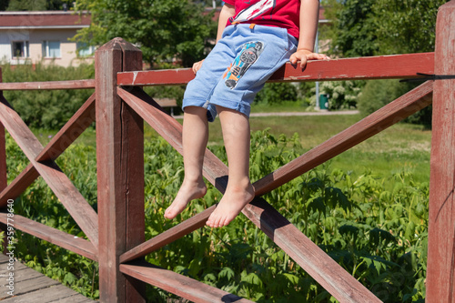 Young boy sits on a fence. Feet close up.