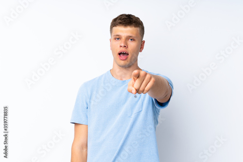 Young handsome man over isolated white background surprised and pointing front
