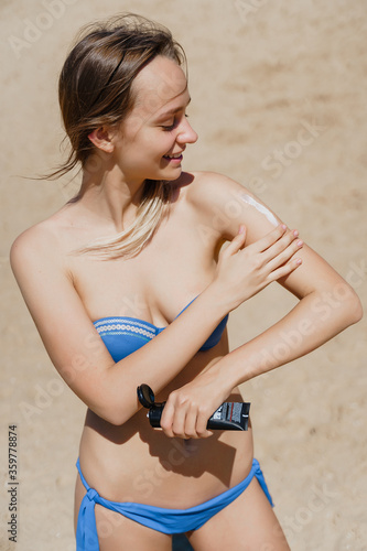 Smiling young woman applying sun cream on beach. Vertical picture. High quality photo