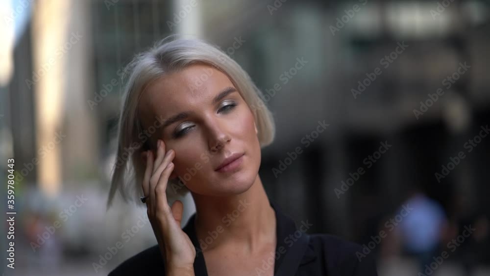 Close-up portrait of a young business girl with short white hair, she is on a city background. She's wearing a black jacket. Poses. Her hair flutters in the wind. Close-up portrait of a young business girl with short white hair, she is on a city background. She's wearing a black jacket. Poses. Her hair flutters in the wind.