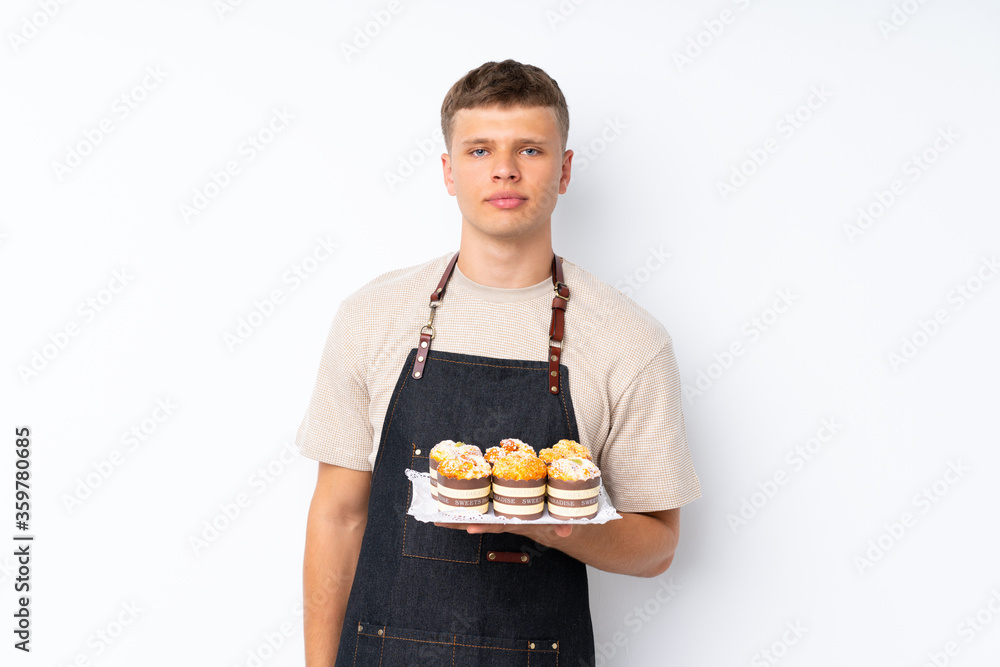 Young handsome man over isolated white background holding mini cakes Young handsome man over isolated white background holding mini cakes