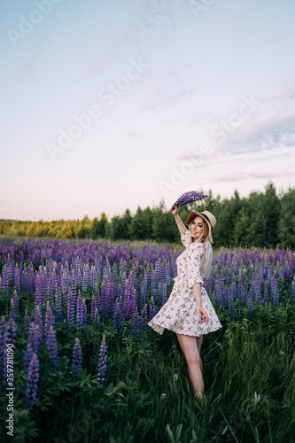 a blonde girl in a dress straw hat holding a bouquet of lupins
