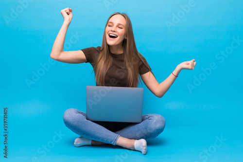 Emotional young woman with laptop celebrating victory on blue background © F8  \ Suport Ukraine