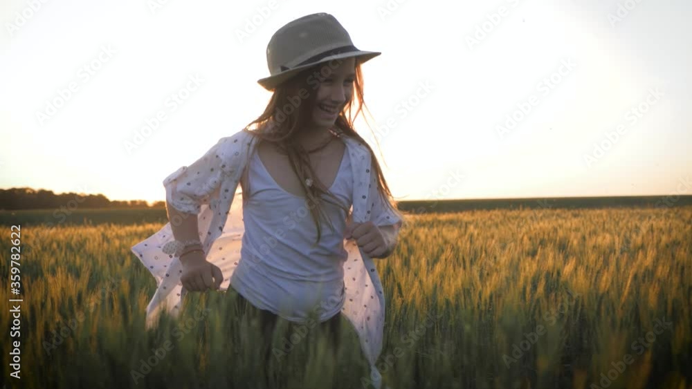 Pretty child in the hat is running across the wheat field. Happy young girl running in the field at sunset. Freedom concept. Pretty child in the hat is running across the wheat field. Happy young girl running in the field at sunset. Freedom concept.