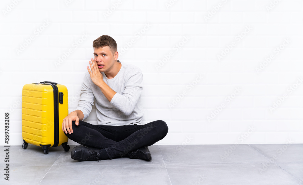 Young handsome man sitting on the floor with a suitcase whispering something Young handsome man sitting on the floor with a suitcase whispering something