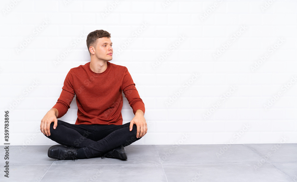 Fototapeta premium Young handsome man sitting on the floor looking to the side