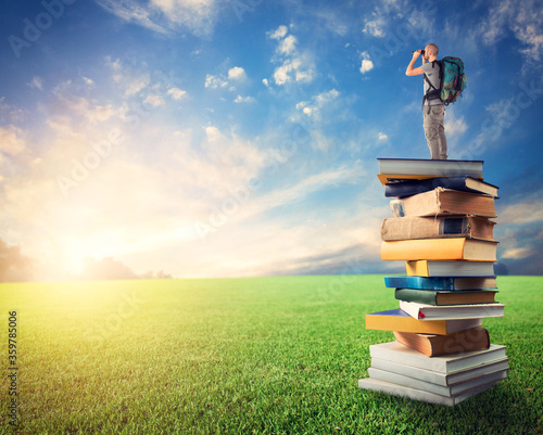 Man with binoculars over a pile of books observe a colorful sunrise. the culture open the imagination