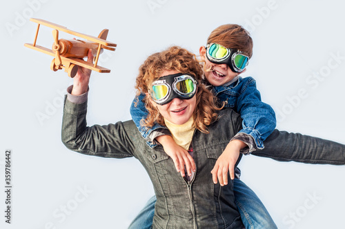 Mom and son wearing pilot glasses imitate pilots, holding a wooden plane in their hands on a white background. The end of the epidemic coronavirus covid-19. Opening borders. Summer travel and tourism