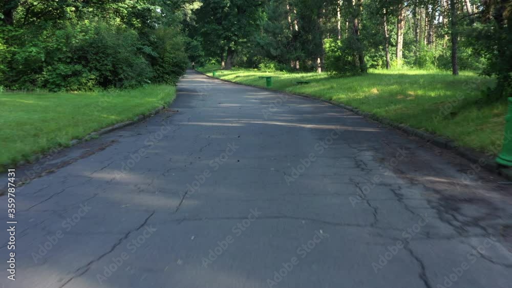 Walk along a asphalt treadmill among the park with trees and grass in the early morning on a sunny warm summer day. POV Walking through the Park. Walk along a asphalt treadmill among the park with trees and grass in the early morning on a sunny warm summer day. POV Walking through the Park.