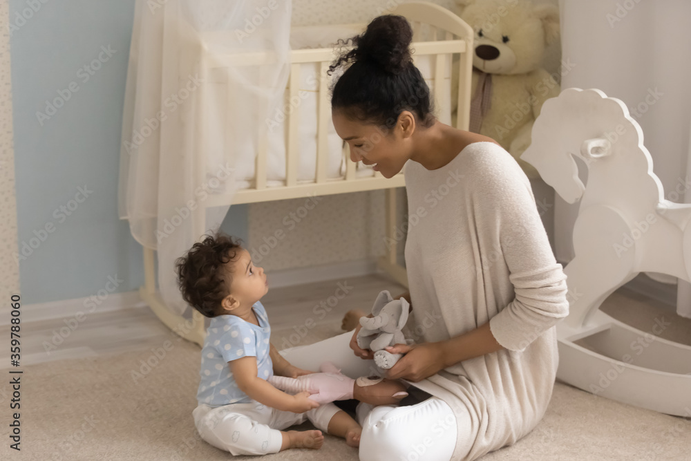 Happy African American mother and cute toddler girl playing with stuffed toys, sitting on warm floor in bedroom at home, loving smiling young mum and little daughter enjoying time together Happy African American mother and cute toddler girl playing with stuffed toys, sitting on warm floor in bedroom at home, loving smiling young mum and little daughter enjoying time together