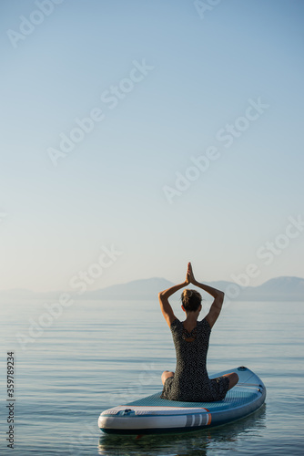 Woman meditating on sup board floating on calm sea water © Gajus