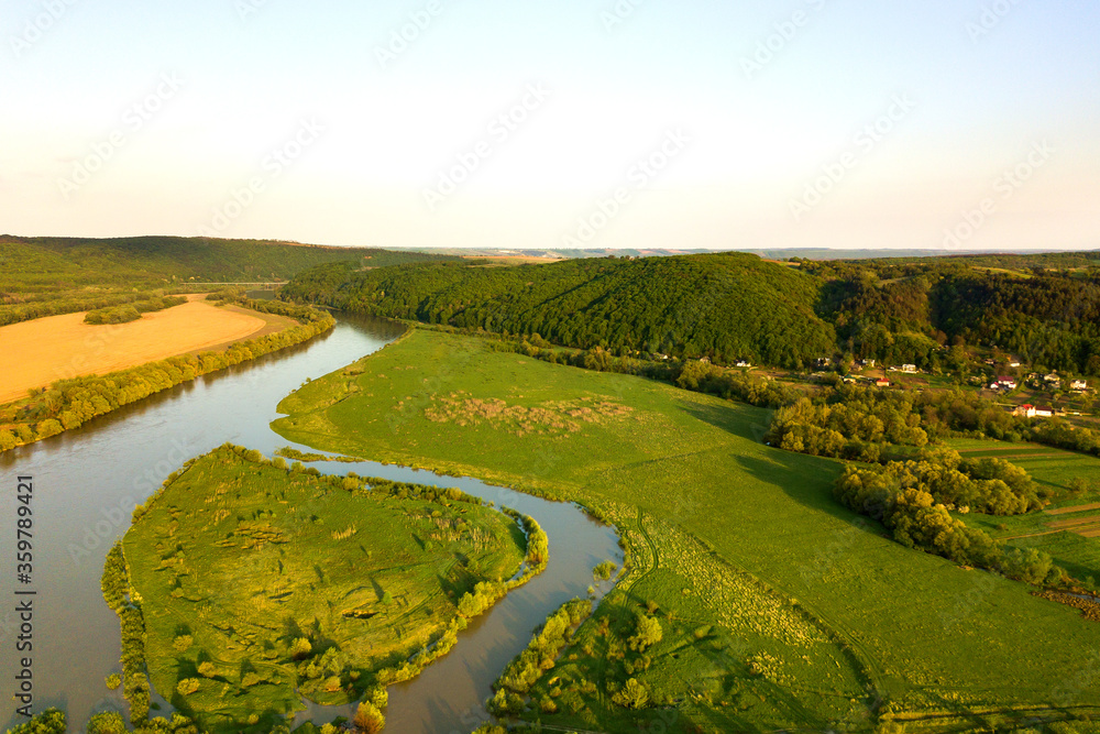 Aerial view of bright river flowing through green meadows in spring.