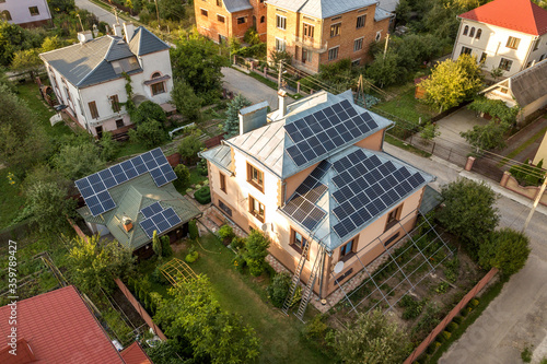 Aerial top view of new modern residential house cottage with blue shiny solar photo voltaic panels system on roof. Renewable ecological green energy production concept.