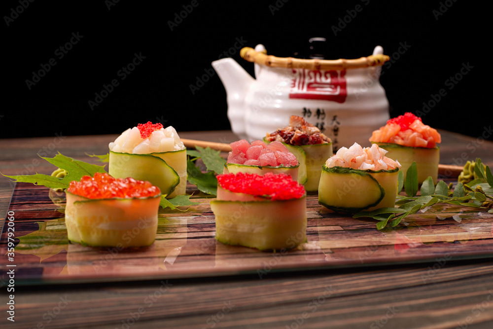 Gunkan maki in a cucumber, with caviar,tuna. scallop, eel, shrimp, eel and salmon, on a wooden board, with maple and acacia leaves, with shallow depth of field Gunkan maki in a cucumber, with caviar,tuna. scallop, eel, shrimp, eel and salmon, on a wooden board, with maple and acacia leaves, with shallow depth of field