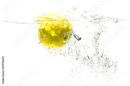 one yellow apple falling into water on a white background with splashes, drops and bubbles.