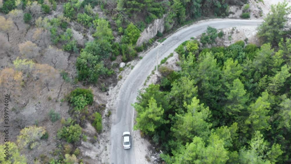 4K Aerial Video View of a Road in the Forest modern car drives along grey asphalt road past dense mixed forest against high hill silhouettes aerial view. 4K Aerial Video View of a Road in the Forest modern car drives along grey asphalt road past dense mixed forest against high hill silhouettes aerial view.