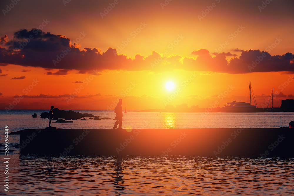 Dramatic sunset over mediterranean sea and silhouette of pier with unrecognizable tourists, romantic mood.