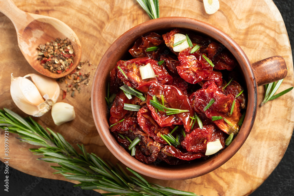 Sun-dried tomatoes with garlic, rosemary and spices in a clay bowl on an olive wood cutting board, top view, flat lay Sun-dried tomatoes with garlic, rosemary and spices in a clay bowl on an olive wood cutting board, top view, flat lay