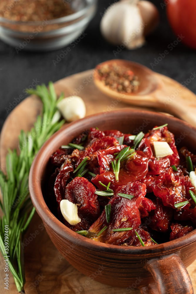 Sun-dried tomatoes with garlic, rosemary and spices in a clay bowl on an olive wood cutting board, vertical image