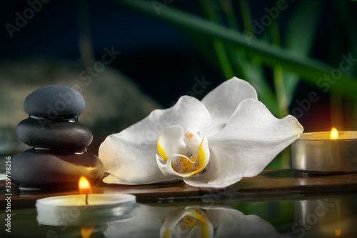 Black zen stones candles and white orchids on a wooden plank on the surface of the water. SPA  relaxation  meditation concept