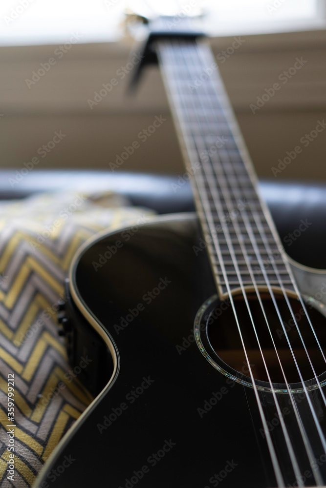 Fototapeta premium Acoustic guitar resting on black leather sofa by the living room window. natural light. 