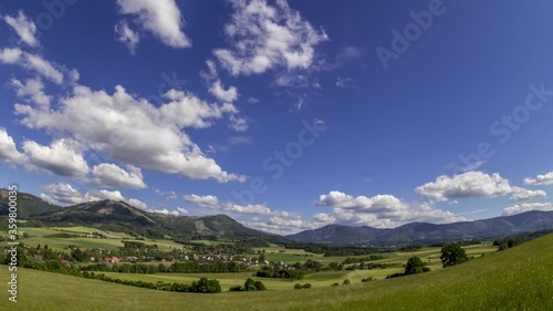 Timelapse wide shot moving to side a mountainous landscape located in area of Beskydy Mountains with lots of peaks during a sunny day with a view of village Kozlovice fast moving clouds in the sky. photo