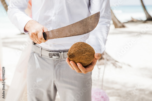 Coconut and hand holding machete for opening. Tropical nut. Caribbean food.
