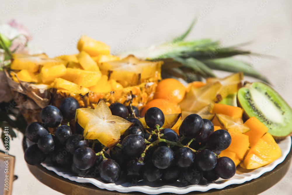 Tropical fruits laying on the dish served on the decorated table staying outdoor at sandy caribbean beach during destination wedding reception ceremony and banquet.Beach catering for outdoors event Tropical fruits laying on the dish served on the decorated table staying outdoor at sandy caribbean beach during destination wedding reception ceremony and banquet.Beach catering for outdoors event