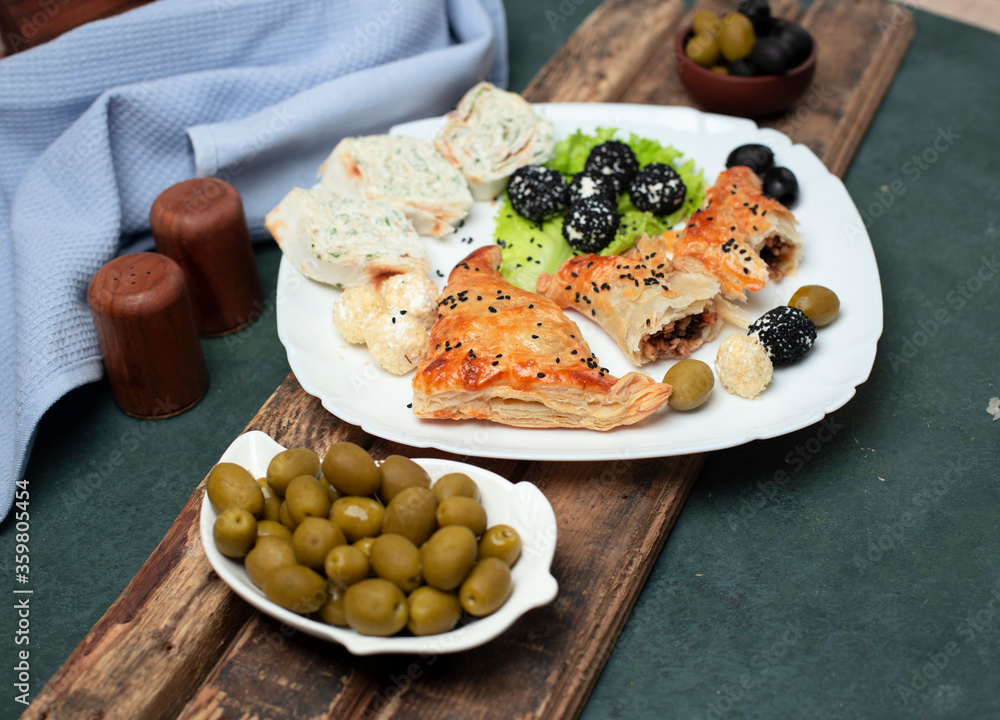 Roll salad with pastry and olives in a white plate on a wooden board