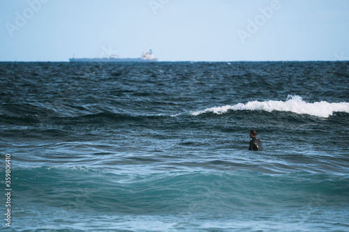 Surfer sitting out the back of the beach, waiting for a wave to catch, peaceful and calm