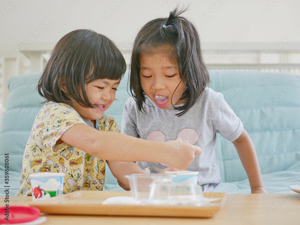 Φωτογραφία Little Asian baby girl ( left ) smiling and enjoys scooping her sister's ice cre