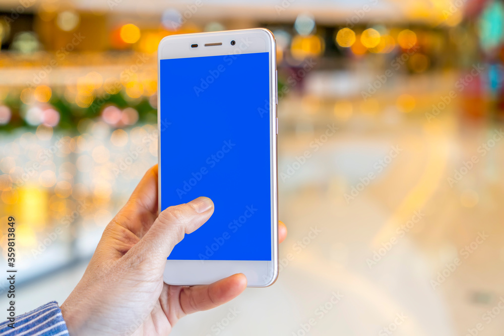 Hand holding smart phone with abstract blur in shopping mall background Hand holding smart phone with abstract blur in shopping mall background