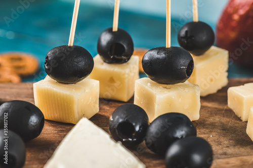 Cheese cubes and black olives on a wooden board with crackers on the blue table