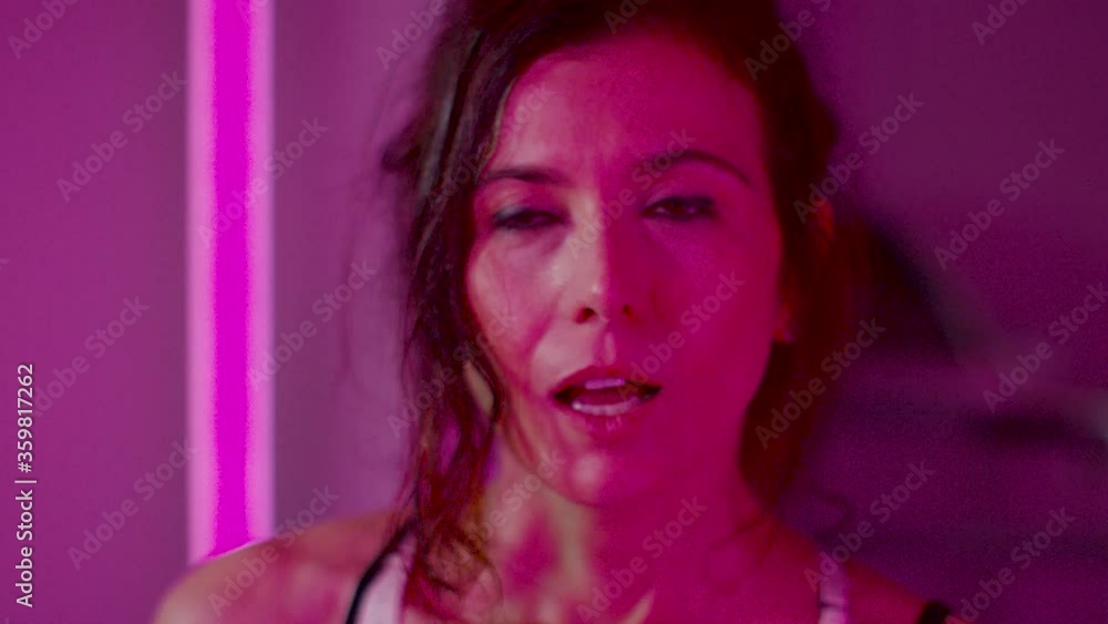 Portrait of Attractive Muscular Woman during Workout. Pink light on the Face. Wipe Sweat in the Gym Portrait of Attractive Muscular Woman during Workout. Pink light on the Face. Wipe Sweat in the Gym